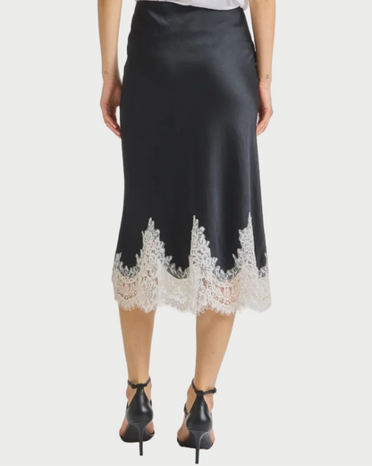 Person wearing a black skirt with lace trim and a white top on a light gray background