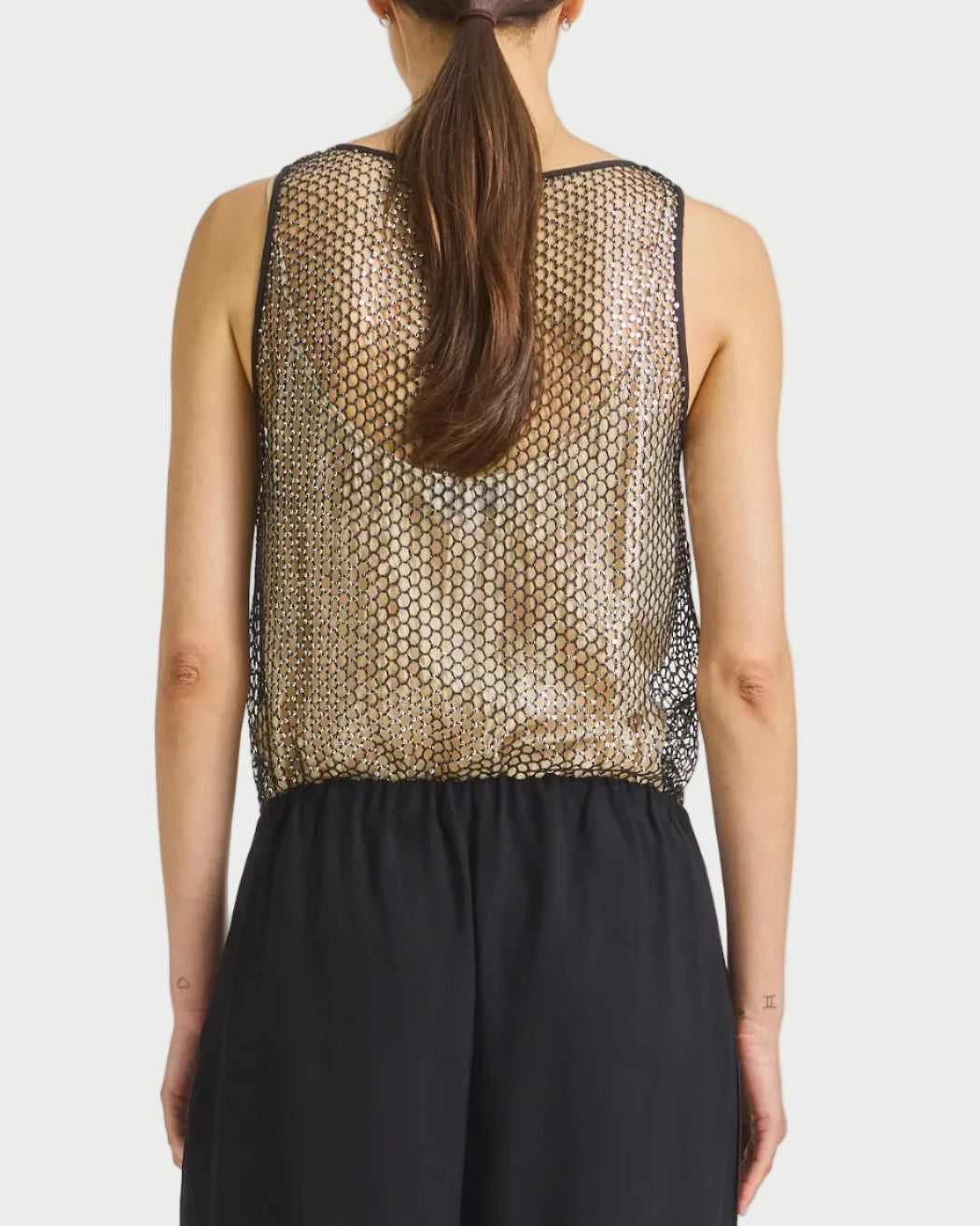 Woman wearing a patterned top and black pants on a plain background