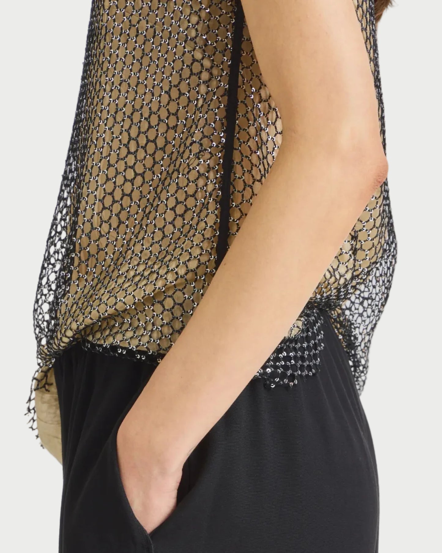 Person wearing a black dress with a sheer black and gold top against a gray background