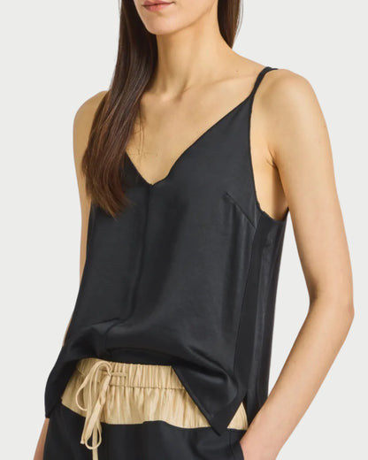 Wearing the Saint Art NY Kiera Tank by Saint Art NY—a black V-neck camisole with thin straps—paired with beige drawstring pants, a woman poses in a mid-face cropped photo that highlights her relaxed style.