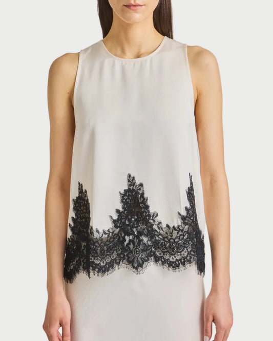 Woman wearing a white sleeveless top with black lace details on a plain background