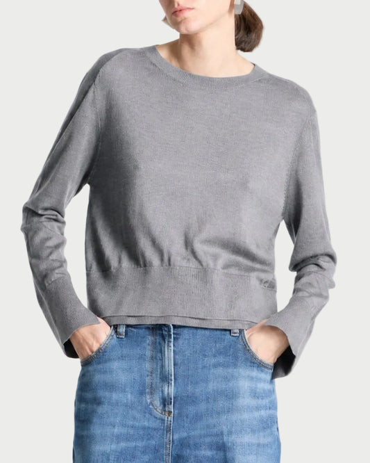 A model wearing a gray long-sleeve knit sweater and blue jeans, standing against a light gray studio background.