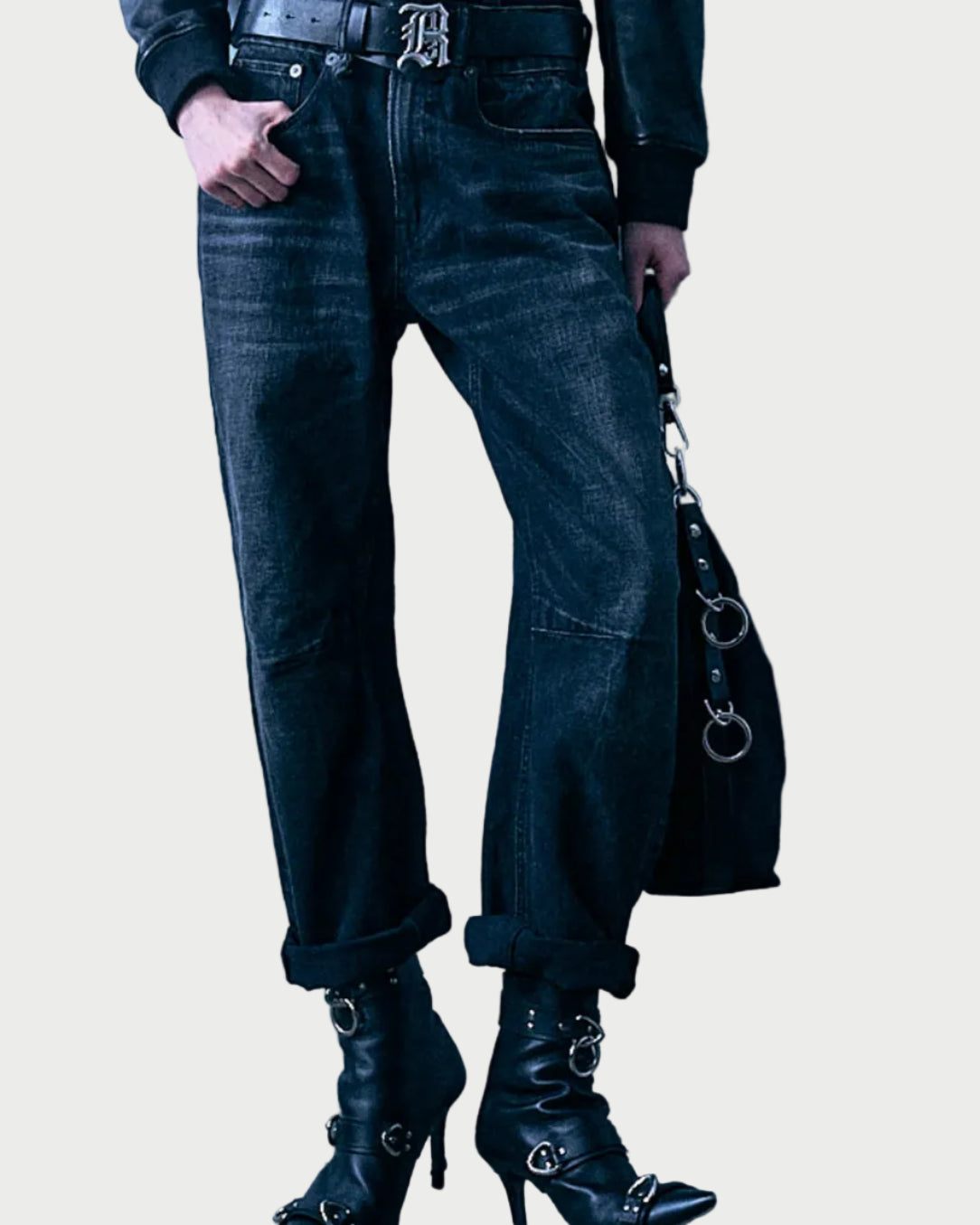 Wearing the R13 Articulated Knee X-BF jeans by R13—crafted from Japanese selvedge denim in a boyfriend fit—paired with a black belt and black heeled boots with silver buckles, and holding a black handbag featuring metal rings. The image is cropped at the waist; upper body and face are not visible.