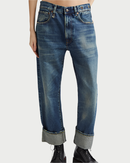 A person wearing the R13 Cuffed X-BF Jean, featuring loose-fitting Italian selvedge denim with a faded wash and cuffed hems, paired with black lace-up shoes, shown waist to feet against a plain background.