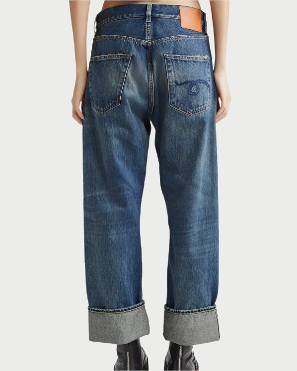 Seen from the back, person wears R13 Cuffed X-BF Jean—loose-fitting, dark indigo jeans with rustic stitching, two rear pockets, cuffed hems, and a brown leather patch on the waistband.