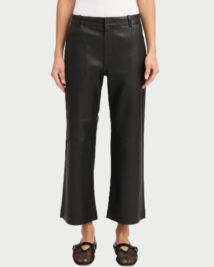 A person stands facing forward against a plain background, wearing SPRWMN Cropped Leather Trousers, a white sleeveless top, and black mesh ballet flats.