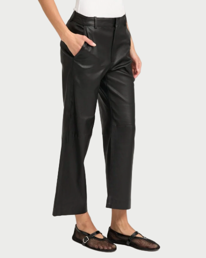 A person wears SPRWMN Cropped Leather Trousers—high-waisted, relaxed fit with a cropped hem—paired with black mesh flats featuring a buckle detail, posing hands-in-pockets against a light background.