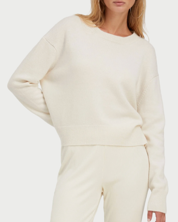 Woman wearing a cream-colored sweater and pants with sunglasses on a white background