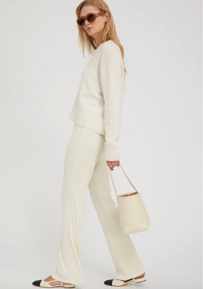 A woman in profile wears the SPRWMN Boxy Cashmere Sweater in Chalk, matching wide-leg pants, sunglasses, and two-tone flats, holding a light beige handbag against a plain white background.