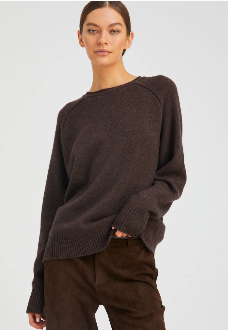 A woman with light skin and brown hair tied back wears the SPRWMN Cashmere Boyfriend Sweater, looking relaxed against a plain light background.