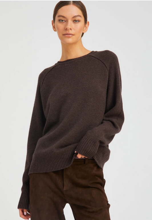 A woman with light skin and brown hair tied back wears the SPRWMN Cashmere Boyfriend Sweater, looking relaxed against a plain light background.