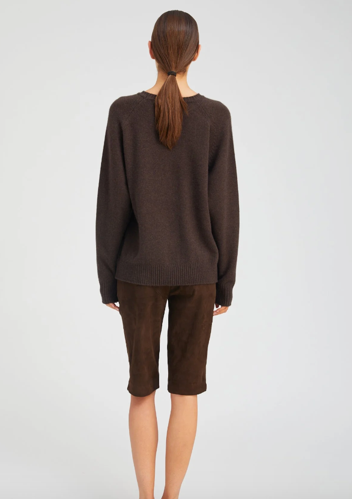 A woman in a SPRWMN Cashmere Boyfriend Sweater and brown shorts.
