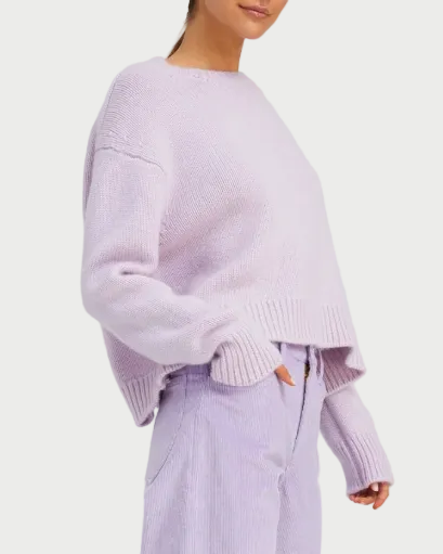 A woman stands against a white background wearing the SPRWMN Heavy Cashmere Crew, an oversized crewneck sweater in light purple, paired with high-waisted, matching light purple pants.