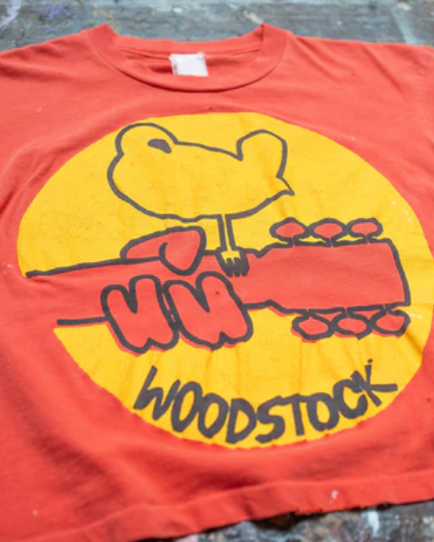Red t-shirt with a graphic of a bear playing guitar and 'Woodstock' text on a textured surface.