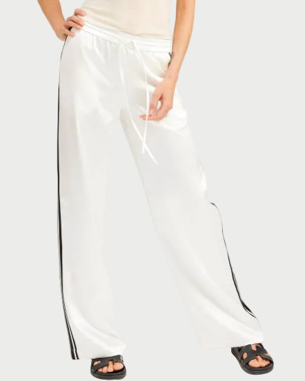 Woman wearing a white tank top and wide-leg pants with a black stripe on a white background