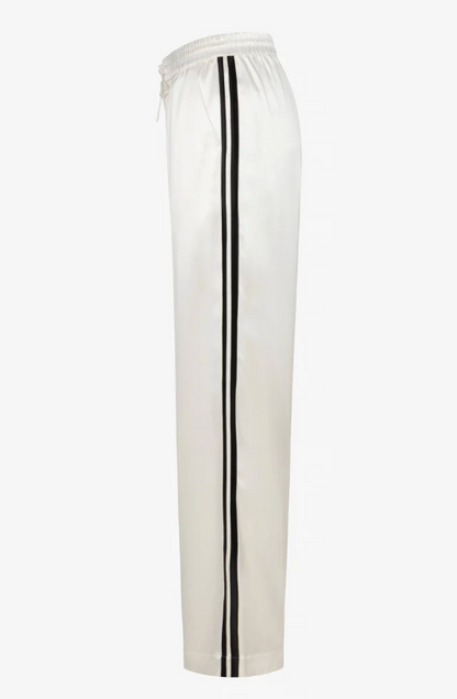 Side view of SPRWMN Baggy Athletic Pant in white satin, featuring a wide-leg fit, elastic waistband, and two black vertical stripes down each leg. Brand: SPRWMN.