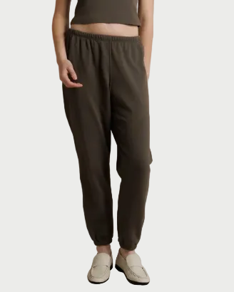 A person is shown from the chest down, standing against a plain background while wearing the perfectwhitetee Johnny French Terry Jogger in dark olive, styled with a matching cropped top and white slip-on shoes.