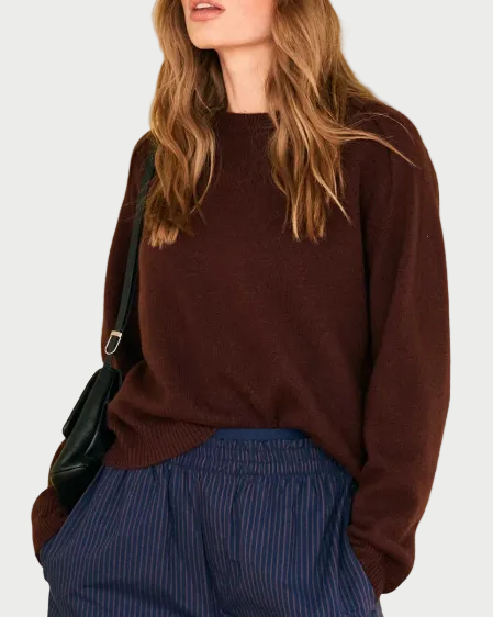 A person wearing a JUMPER1234 Oversize Cashmere Crew Cocoa in dark brown, styled with navy pinstriped trousers and a black shoulder bag.