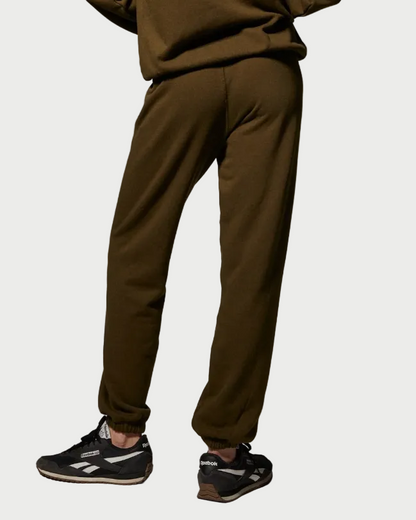 A person wearing olive green SPRWMN Heart Sweatpants with elastic cuffs and black sneakers.
