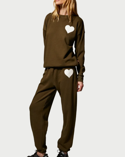 A person wearing a relaxed fit, olive green SPRWMN Heart Sweatshirt and matching sweatpants, both featuring a white heart patch.