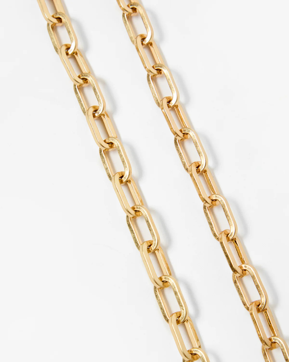 A close-up of a gold paperclip chain necklace draped diagonally on a clean white background.