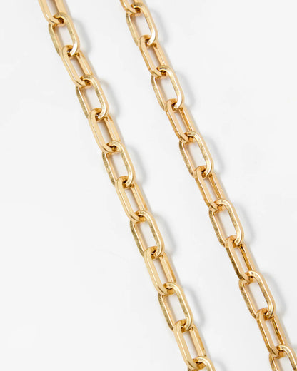 A close-up of a gold paperclip chain necklace draped diagonally on a clean white background.