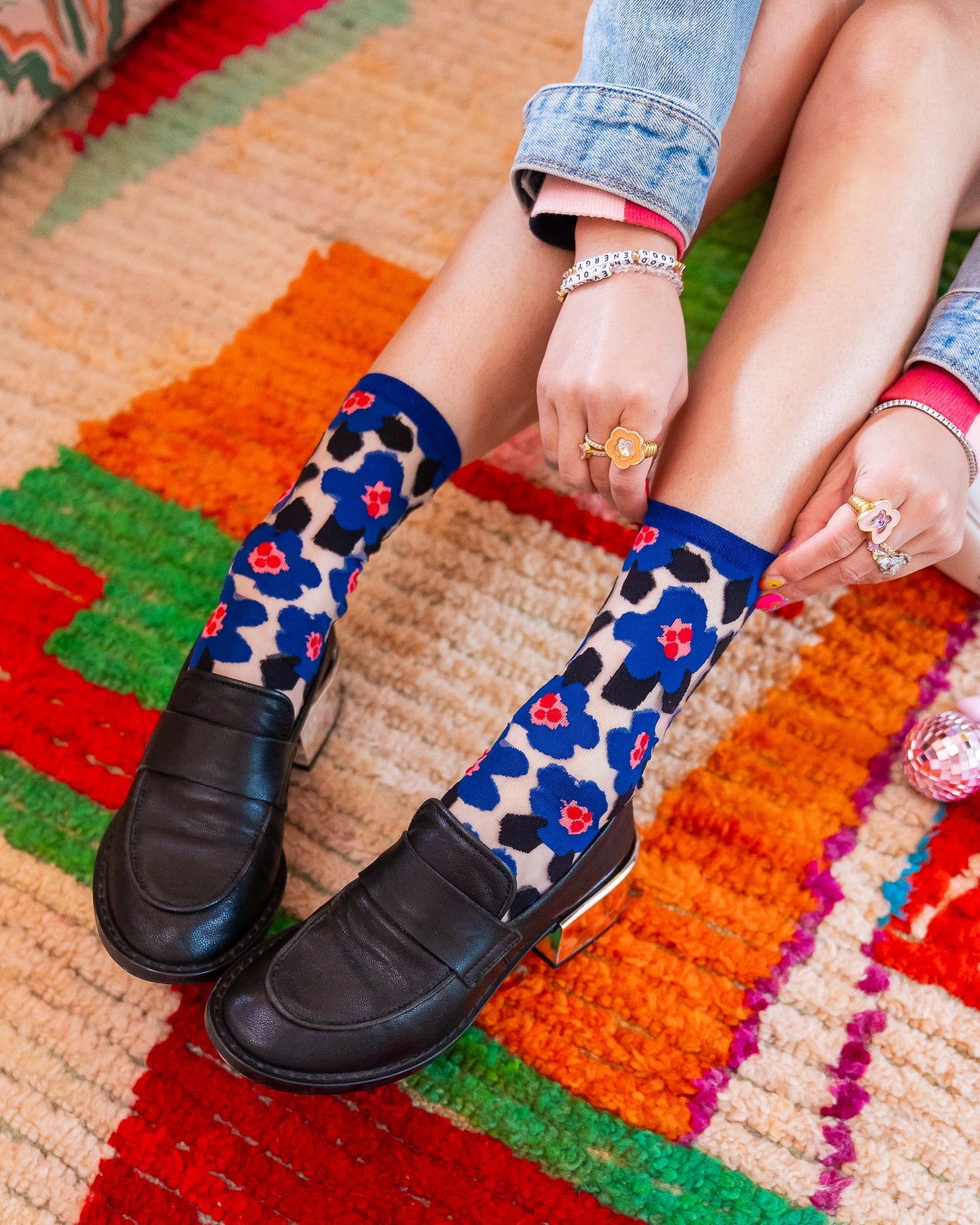 Person wearing blue floral socks with black shoes on a colorful rug