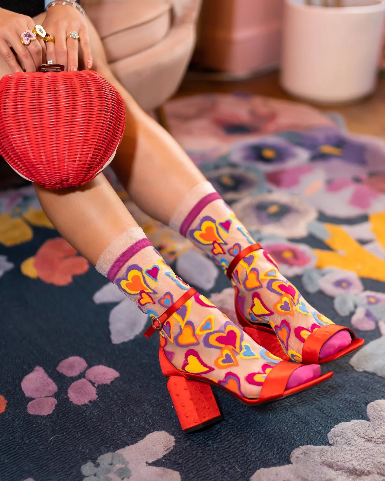 Colorful heart-patterned shoes worn with a red bag on a patterned rug.