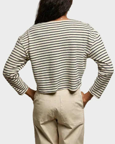 A person stands with their back to the camera, hands in their pockets, wearing the perfectwhitetee Taylor Stripe Long Sleeve—this versatile top features black horizontal stripes and is styled with light beige pants.