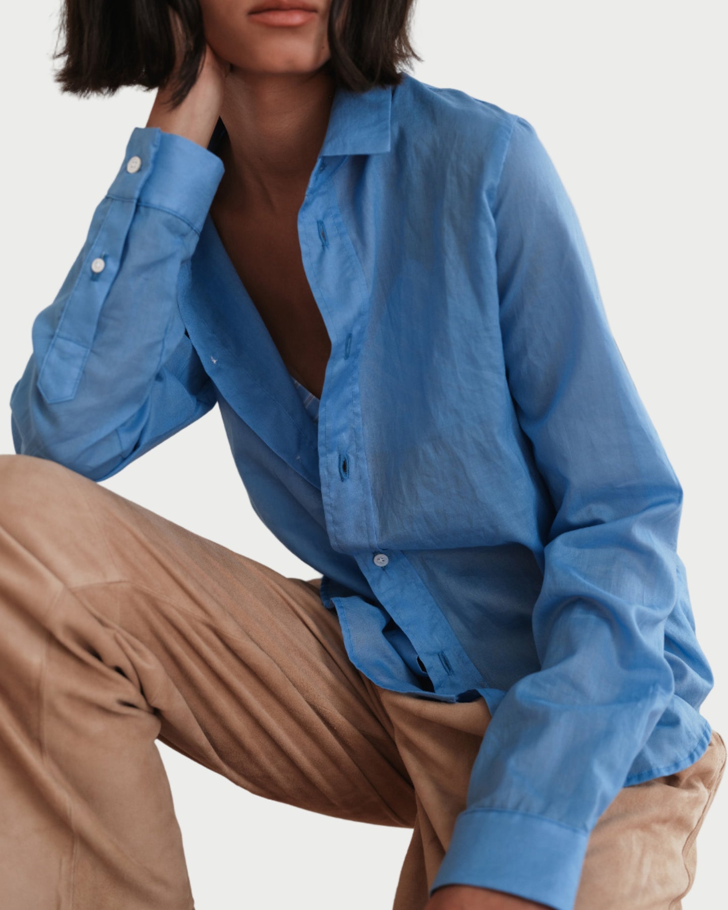 Person wearing a blue shirt and beige pants sitting on a wooden chair.