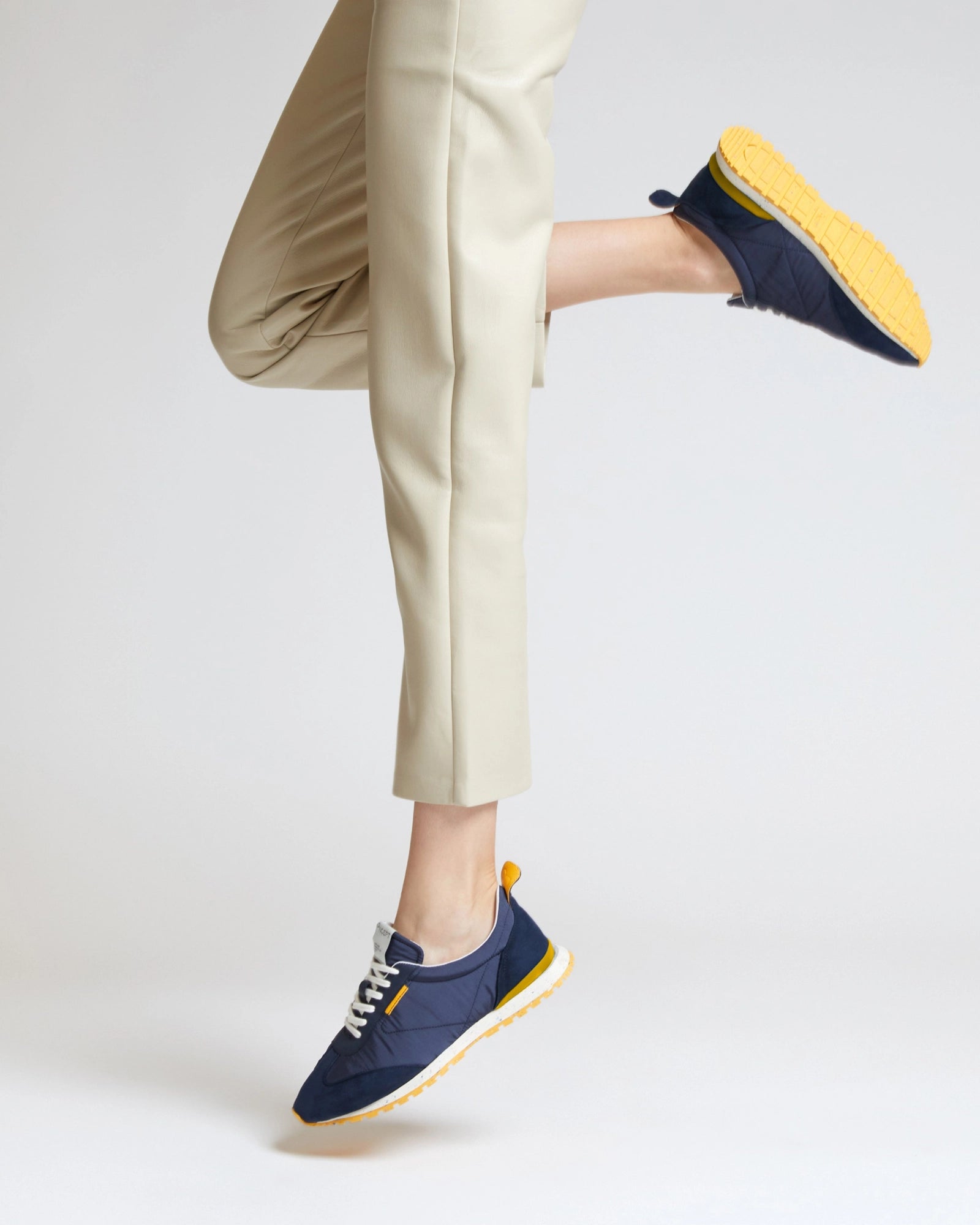 Person wearing navy sneakers with yellow soles on a light background