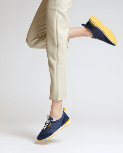 Person wearing navy sneakers with yellow soles on a light background