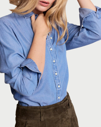 Woman wearing a blue denim shirt with rolled-up sleeves against a plain background