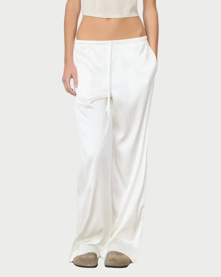 Woman wearing a beige top and white pants against a plain background