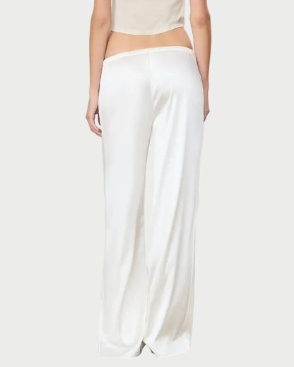 Person wearing a beige top and white pants against a plain background