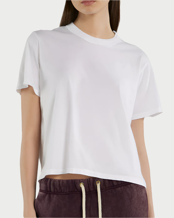 A woman wears the Les Tien Jane Classic White Tee, a relaxed fit cotton top, paired with burgundy drawstring pants. She is shown from shoulders to hips against a light background.