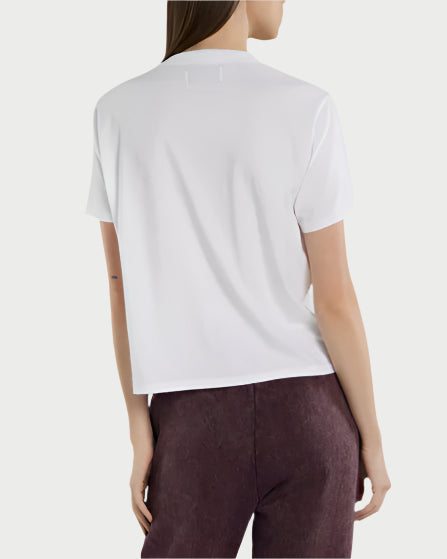 A woman with long straight hair stands against a light background, shown from the back in a relaxed fit Les Tien Jane Classic Tee in plain white and high-waisted dark reddish-brown pants.