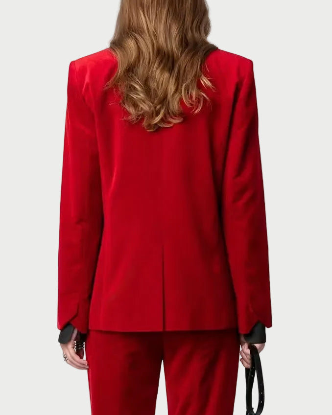 A woman shown from the back wearing a bright red tailored pantsuit with a structured blazer and matching flared trousers, holding a small black handbag against a plain light background.