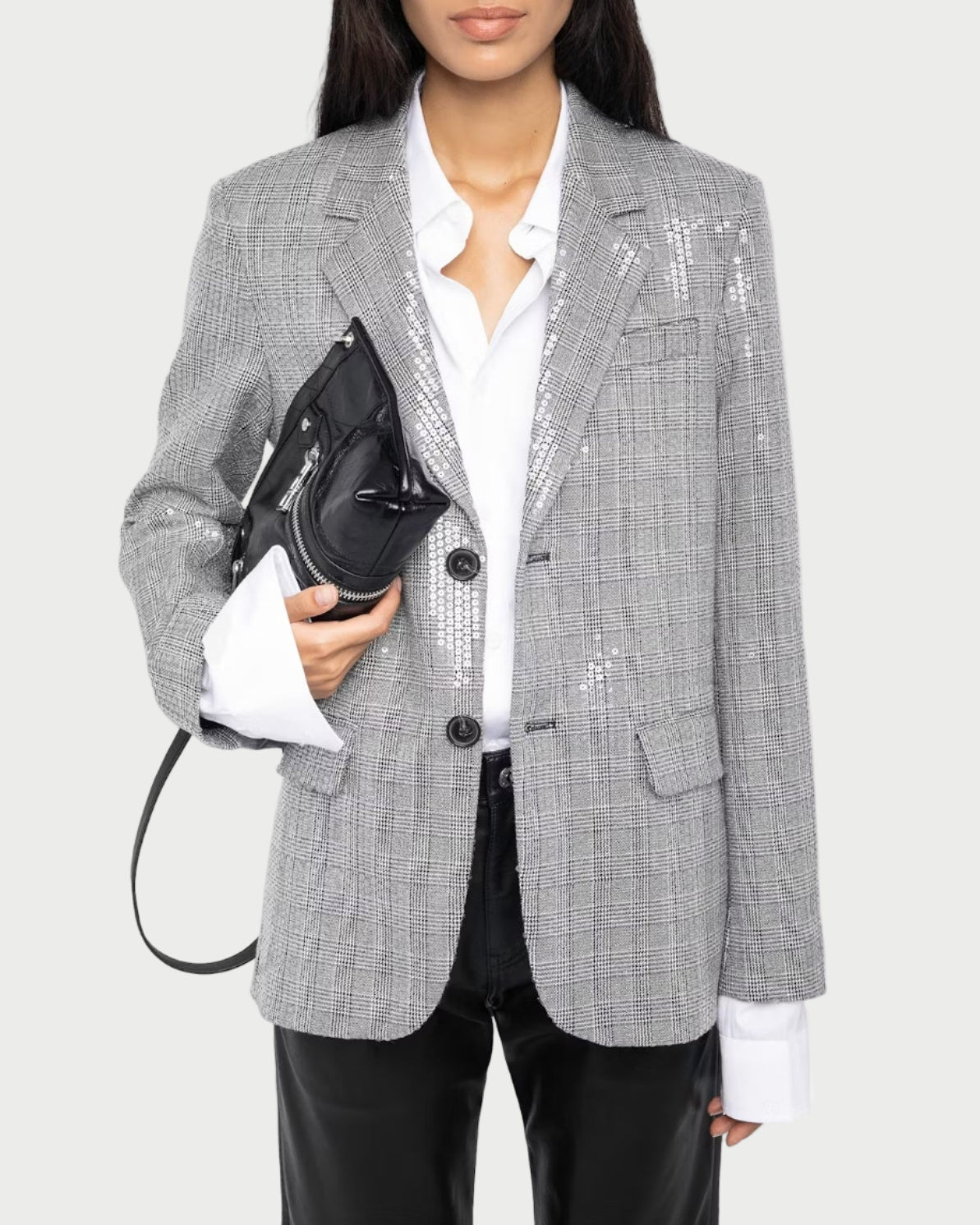 Person wearing a gray checkered blazer with sequin details, holding a black handbag on a white background.