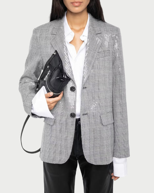 Person wearing a gray checkered blazer with sequin details, holding a black handbag on a white background.