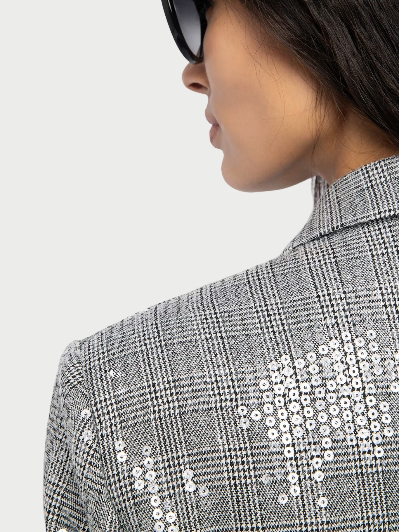 Person wearing a gray checkered jacket with white sequin details on a plain background