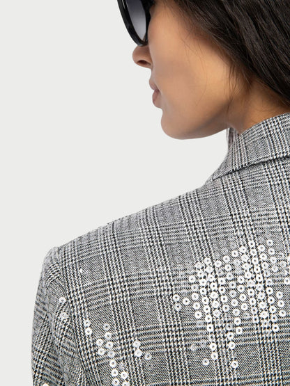 Person wearing a gray checkered jacket with white sequin details on a plain background