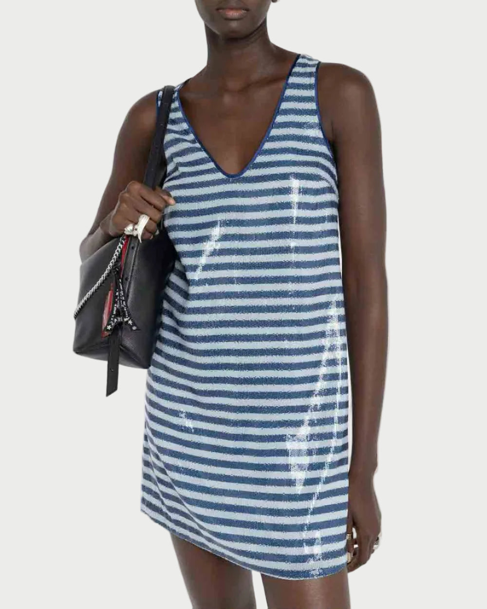 Woman wearing a blue and white striped dress holding a black bag on a plain background