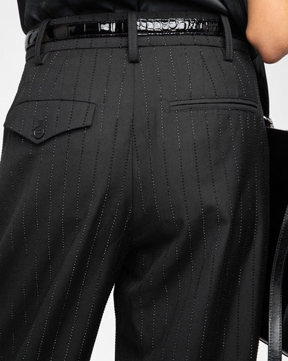 Black pinstripe pants with a belt on a neutral background