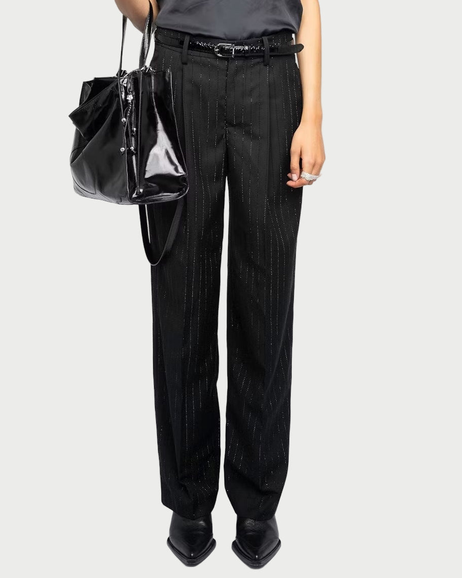 Person wearing a black sleeveless top and black pants holding a black handbag on a white background