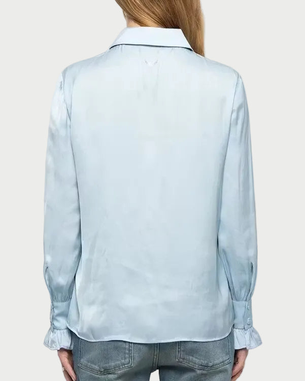 A woman viewed from behind wearing a light blue long-sleeve button-up shirt and blue jeans against a plain light gray studio background.