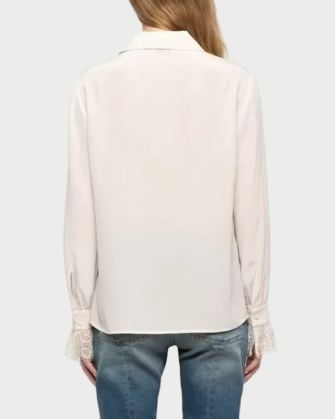A woman viewed from the back wearing a light cream long-sleeve blouse and blue flare jeans against a plain light gray studio background.