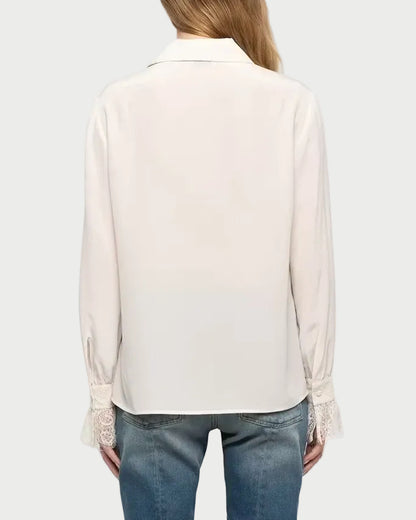 A woman viewed from the back wearing a light cream long-sleeve blouse and blue flare jeans against a plain light gray studio background.
