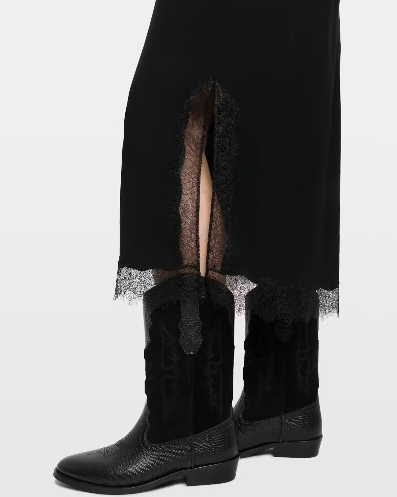 Black lace skirt with a side slit, paired with black leather cowboy boots, photographed against a light gray studio background.