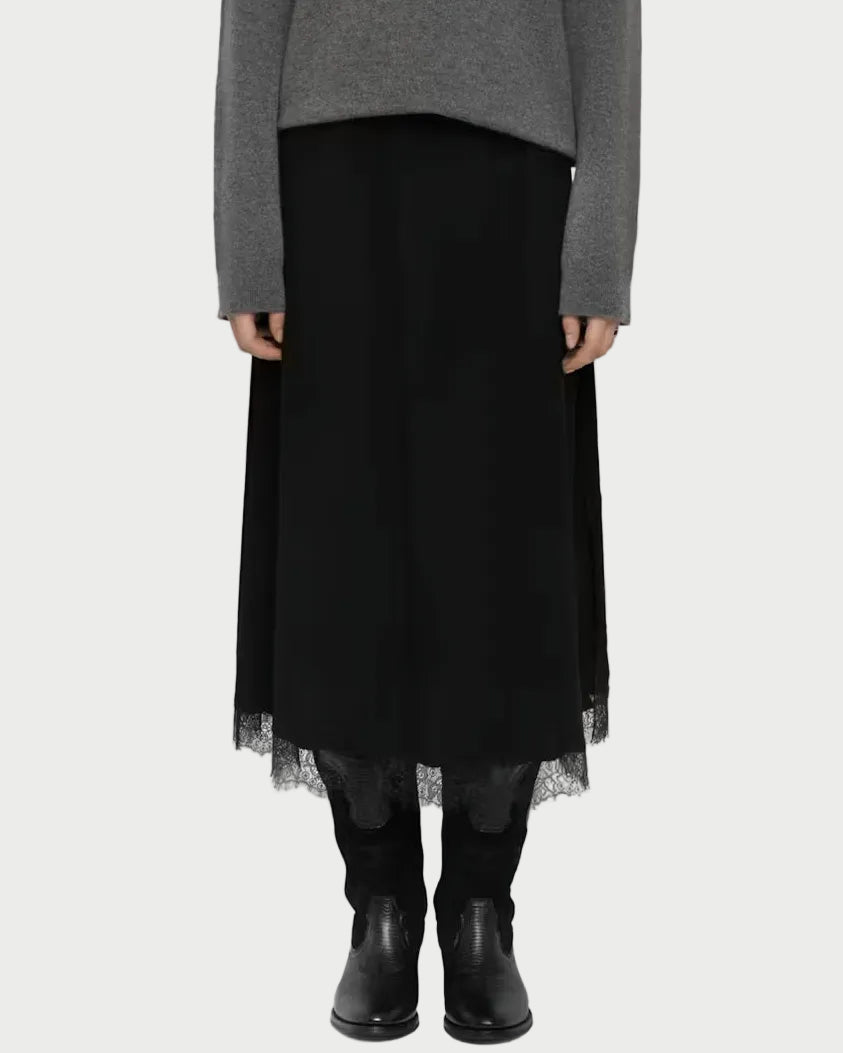 A model stands against a light gray studio background wearing a gray knit sweater, a long black skirt with a sheer tulle hem, black leggings, and black ankle boots.
